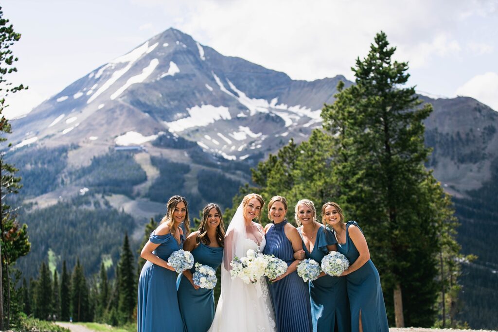 A radiant bride and her bridesmaids pose with bouquets against the stunning mountain backdrop of Big Sky Resort.