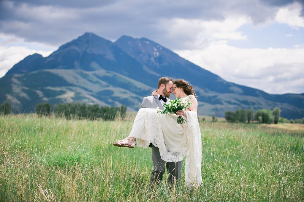 Bride and groom in a romantic embrace in front of a breathtaking mountain backdrop at Sage Lodge, Montana.